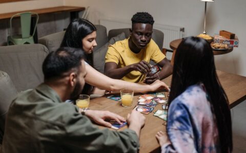 A diverse group of friends playing a strategic card game while enjoying drinks indoors.