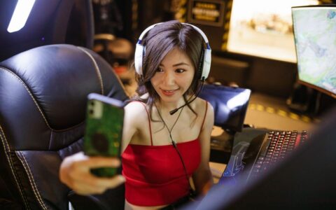 A young woman gamer with headphones taking a selfie during a gaming session.