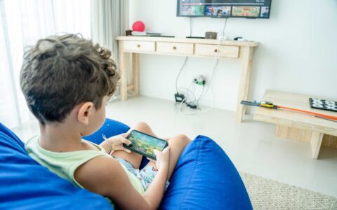 A young boy sitting on a bean bag playing a game on his smartphone in a modern living room.