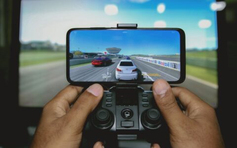 Close-up of hands playing a racing game on a mobile device with a controller.