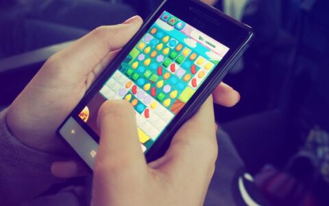 Hands holding a smartphone with a colorful puzzle game on the screen, displaying modern technology.