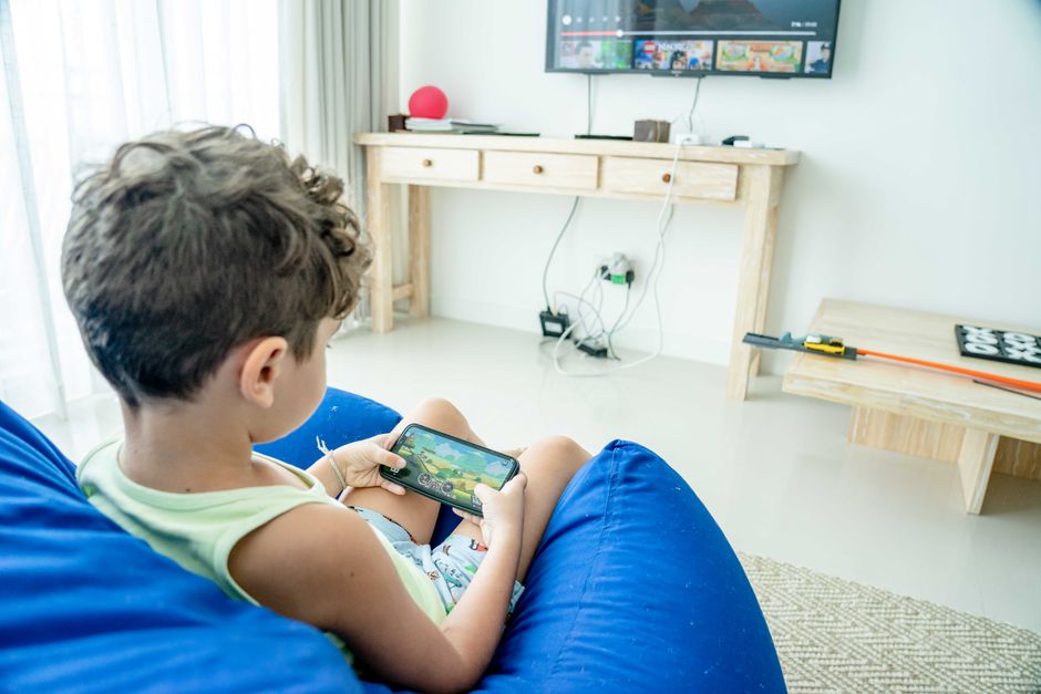 A young boy sitting on a bean bag playing a game on his smartphone in a modern living room.