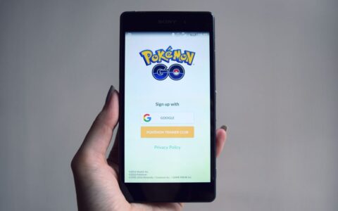 Smartphone displaying Pokémon Go app sign-in screen, held in hand.