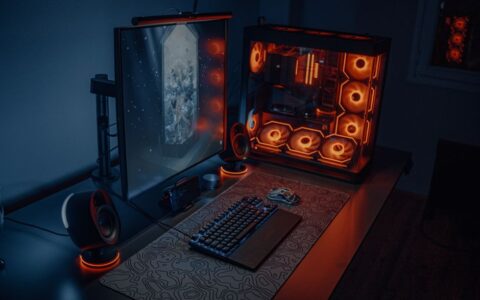 Sleek gaming desk setup featuring RGB lighting, large monitor, and gaming PC with glowing fans.
