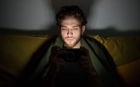Focused young man looking at a smartphone screen, creating a moody atmosphere indoors.