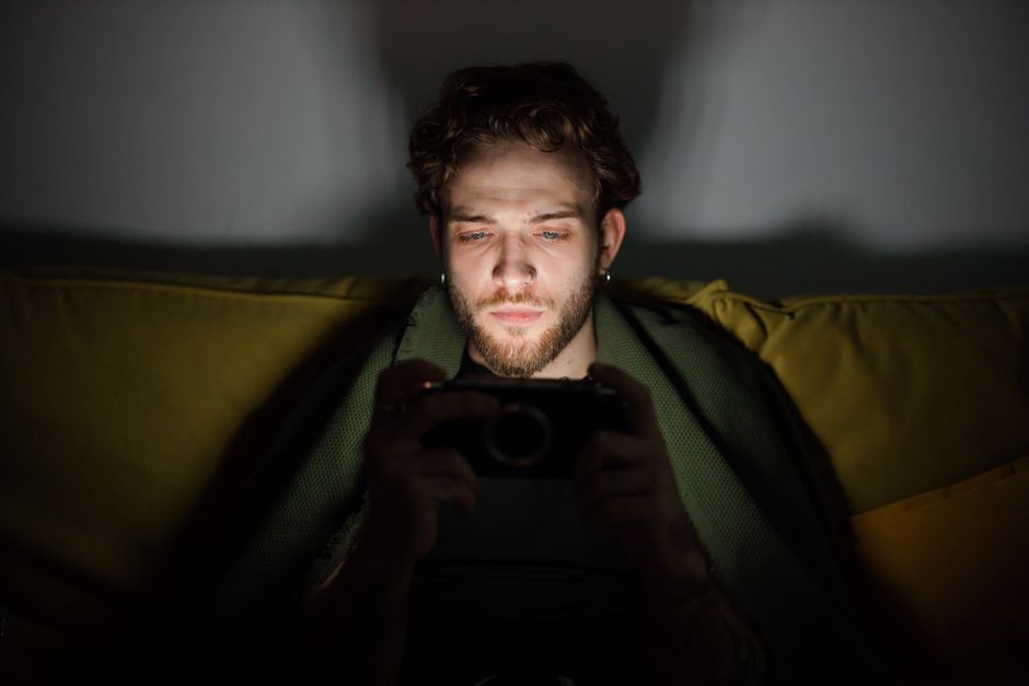 Focused young man looking at a smartphone screen, creating a moody atmosphere indoors.
