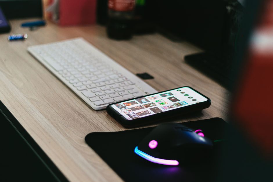 A sleek desktop setup featuring a smartphone, keyboard, and vibrant RGB mouse.