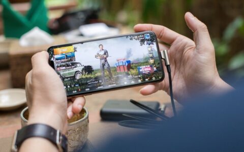 Person playing PUBG on smartphone outdoors with charging cable attached.